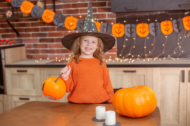 Little girl at home in the kitchen at the table with a pumpkin for halloween