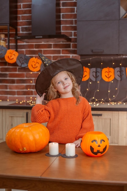 Little girl at home in the kitchen at the table with a pumpkin for halloween