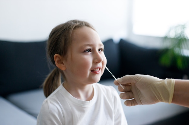 Little girl at home during taking nasal mucus test sample from nose performing respiratory virus testing procedure showing Covid-19