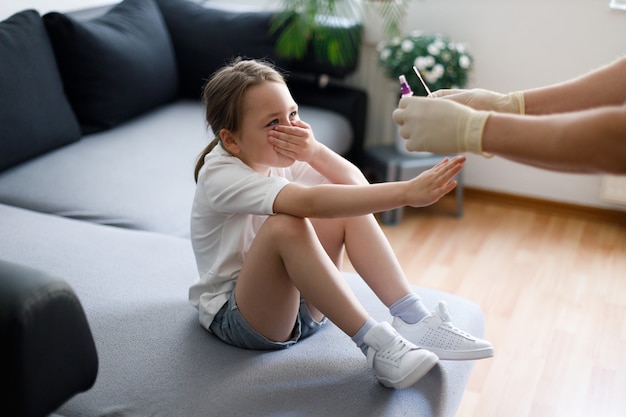 Little girl at home during taking nasal mucus test sample from nose performing respiratory virus testing procedure showing Covid-19