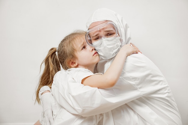 A little girl hugs a doctor in a white protective suit, mask, glasses and gloves.