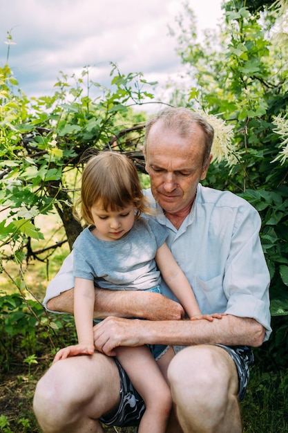 A little girl hugs her grandfather on a walk in the summer outdoors