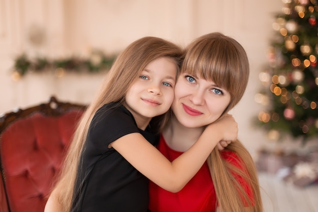 Little girl hugs her mom near the Christmas tree