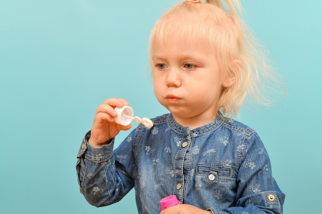 Little girl inflates soap bubbles on a blue background