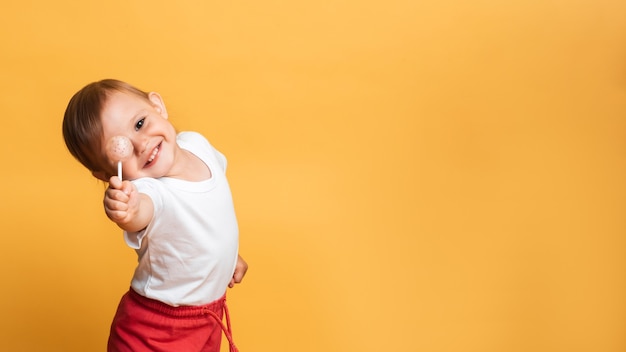 A little girl is eating a sweet lollipop on a stick. Yellow background. The concept of prevention of caries and diabetes in children. Place for your text