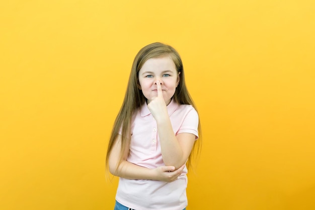 Little girl is funny smiles and shows a pig nose on a yellow background