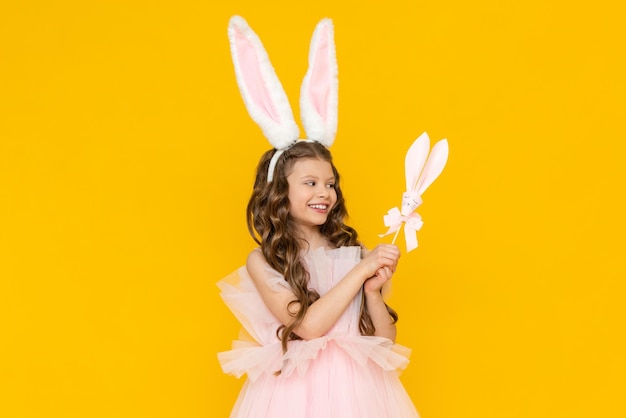 A little girl is happy about Easter Happy spring holiday for children A child with rabbit ears on his head A teenage girl with curly hair on a yellow isolated background