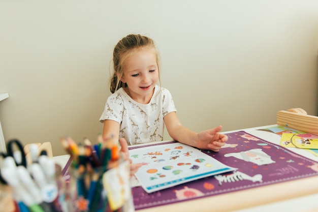 A little girl is happy to learn while sitting at his desk. Homeschool concept. Education concept. Kid learning background. Toddler handmade game. Kindergarden education.