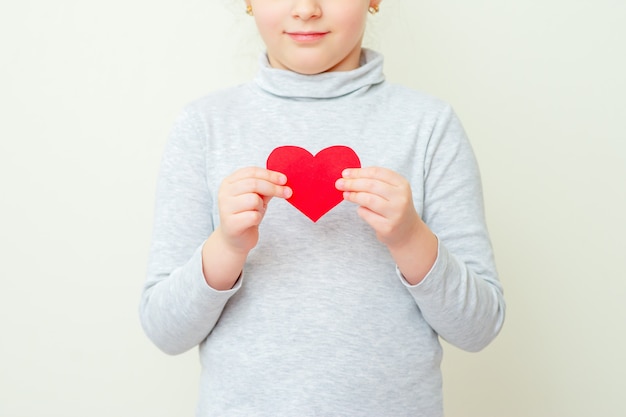 Little girl is holding red little heart.