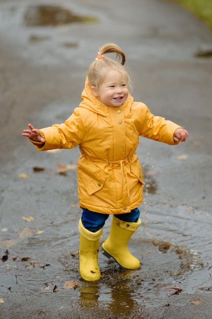 A little girl is jumping in a puddle in yellow rubber boots and a waterproof raincoat Autumn Walk