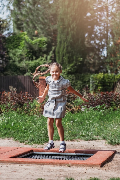 Little girl is jumping on trampoline in a park Happy laughing kid outdoors in the yard on summer vacation Jump high