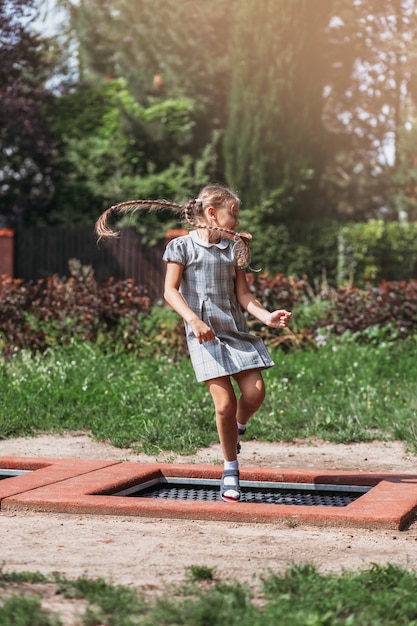 Little girl is jumping on trampoline in a park Happy laughing kid outdoors in the yard on summer vacation Jump high