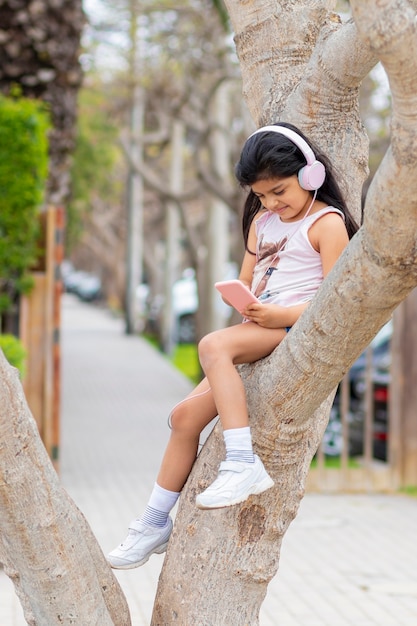 Little girl is listening to music with her headphones on a tree