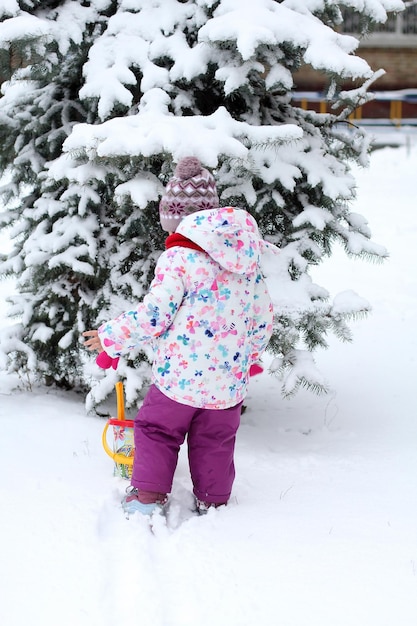 A little girl is playing in the snow near the Christmas tree in the yard