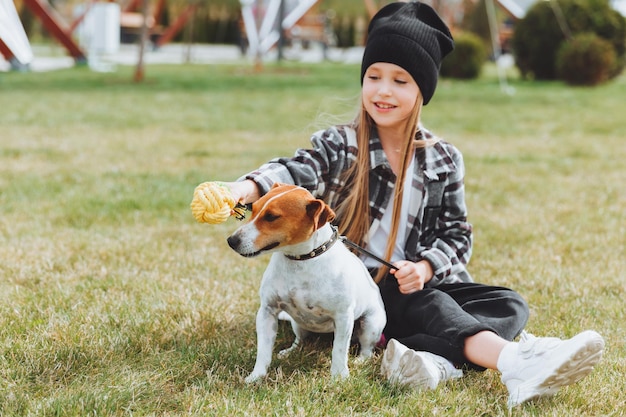 A little girl is playing with her dog on the grass in the park jack Russell terrier a child gives a toy to his dog