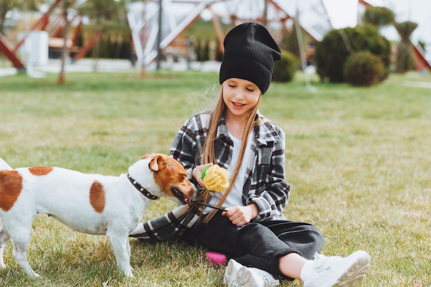 A little girl is playing with her dog on the grass in the park jack Russell terrier a child gives a toy to his dog