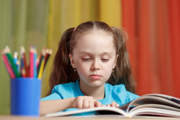 Little girl is reading a book sitting at a table