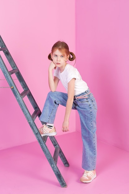 A little girl is sitting on a gray staircase on a pink background in the studio