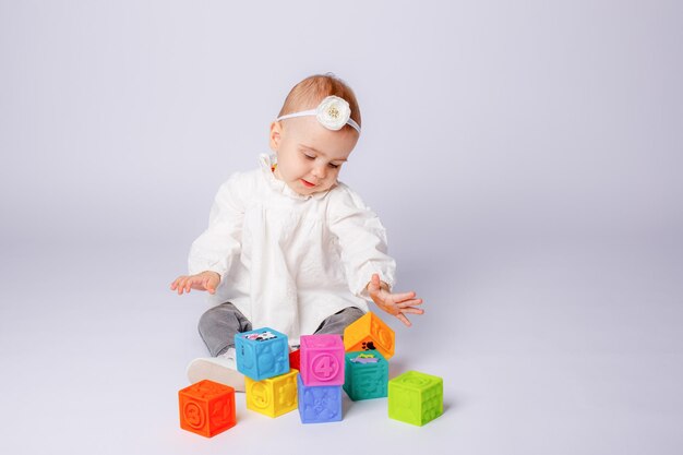 a little girl is sitting playing with multicolored cubes  isolated on a white background