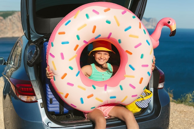 Little girl is sitting in the trunk of a car and holding a huge inflatable circle in her hands