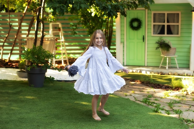 Little girl is spinning barefoot in dance on ground in white dress in summer garden  in backyard