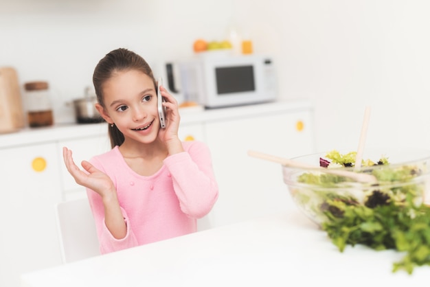 Little girl is talking on the phone in the kitchen.