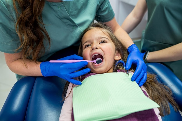 A little girl is treated for small teeth in a dental chair by a qualified pediatrician