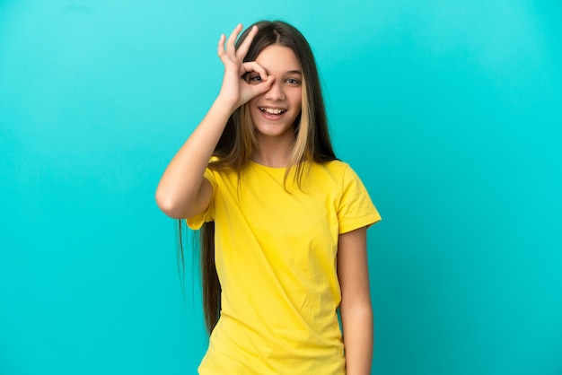 Little girl over isolated blue background showing ok sign with fingers