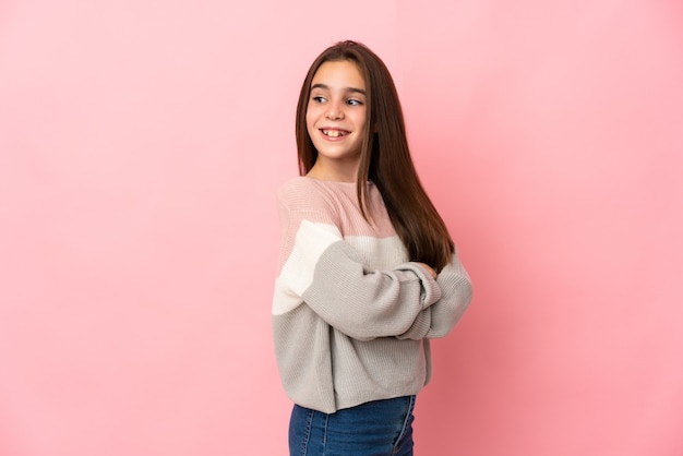 Little girl isolated on pink background with arms crossed and happy