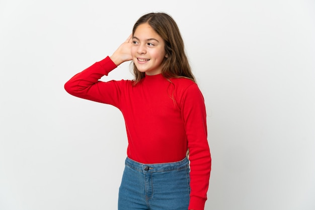 Little girl over isolated white background listening to something by putting hand on the ear