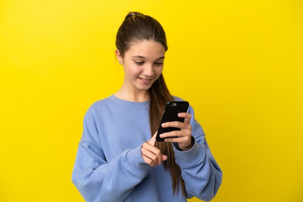 Little girl over isolated yellow surface sending a message or email with the mobile