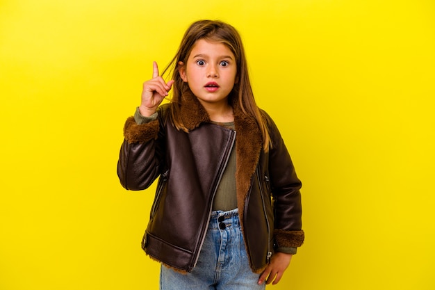 Little girl isolated on yellow wall having an idea