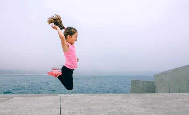 Little girl jumping outdoors by sea pier