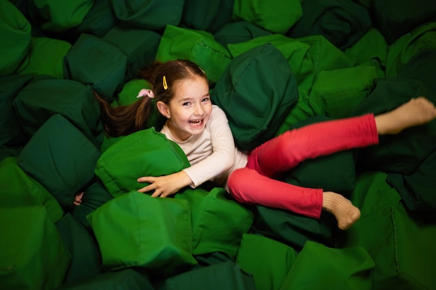 Little girl kid lies on green soft cubes at playground park Child in active entertaiments