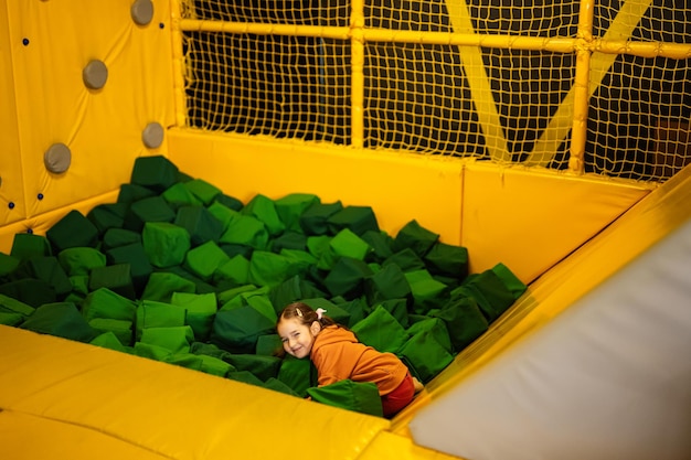 Little girl kid slide to green soft cubes at yellow playground park Child in active entertaiments