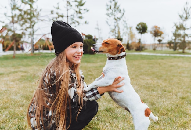 A little girl kisses and hugs her Jack Russell terrier dog in the park Love between the owner and the dog a child is holding a dog in his arms