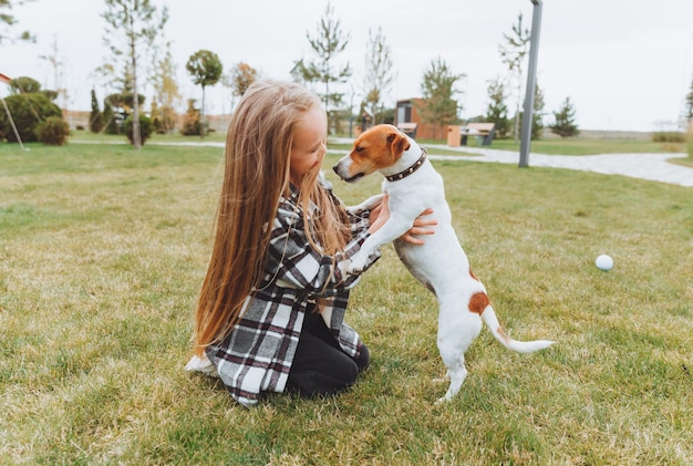 A little girl kisses and hugs her Jack Russell terrier dog in the park Love between the owner and the dog a child is holding a dog in his arms