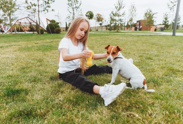 A little girl kisses and hugs her Jack Russell terrier dog in the park Love between the owner and the dog a child is holding a dog in his arms