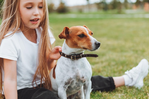 A little girl kisses and hugs her Jack Russell terrier dog in the park Love between the owner and the dog a child is holding a dog in his arms