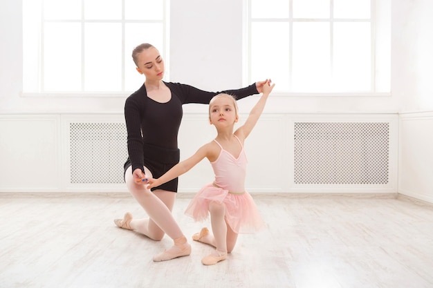 Little girl learning ballet with teacher copy space. Cute small ballerina training classical dance exercises with female coach.