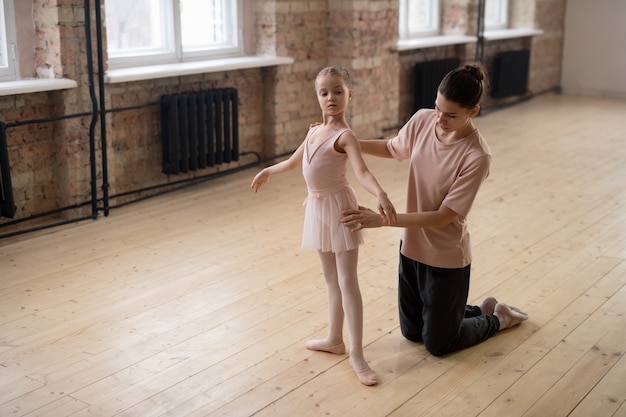 Little girl learning to stand in right position during her ballet classes with trainer