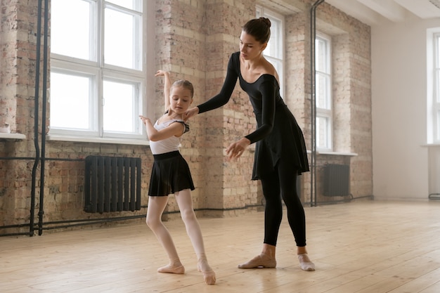 Little girl learning to stand in right position during her ballet classes with trainer