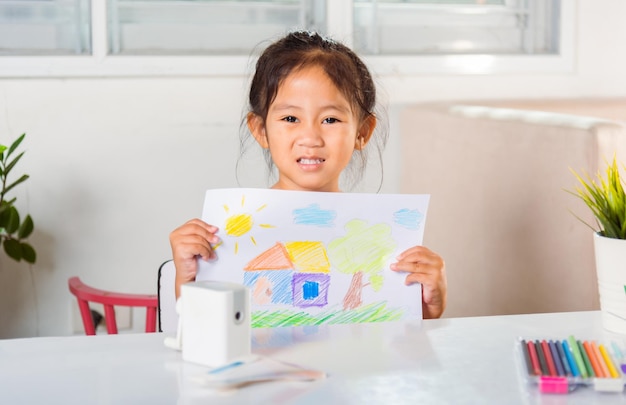 Little girl lift up colorful drawing landscape my home dream on paper to camera