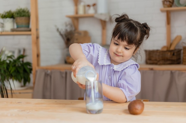 little girl in a lilac dress drinks milk and eats a bun at the kitchen table. space for text, banner