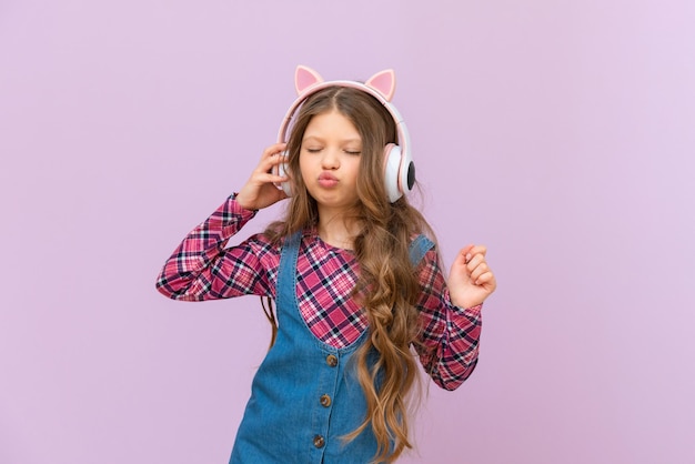 A little girl listens to music with headphones a child on an isolated background in pink headphones