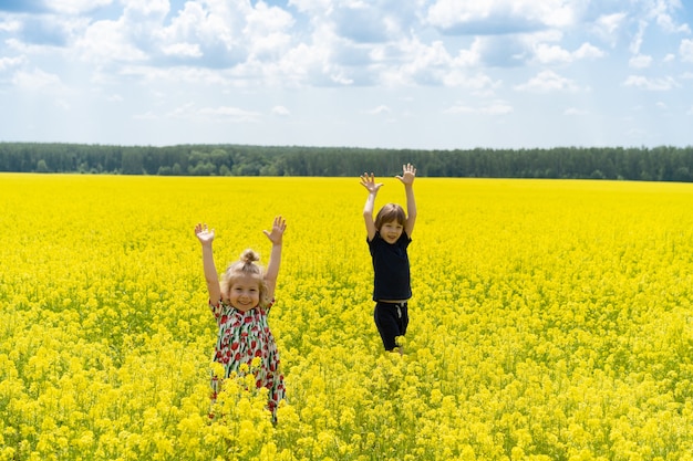 Little girl and little boy in rapeseed field, brother and sister in flower field in summer.