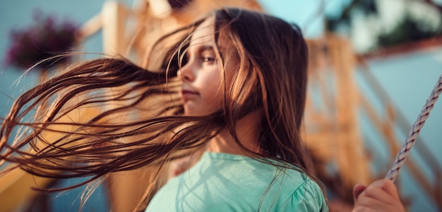 Little girl long hair flying in the air while she sitting on swing