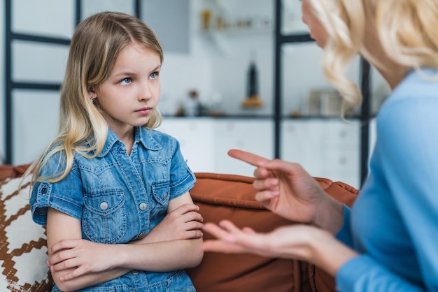 Little girl looking sad while her mother scolding her sitting on couch at home