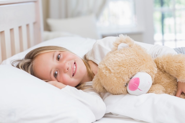 Little girl lying in her bed holding her teddy 