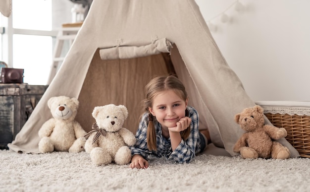 Little girl lying in wigwam with teddies